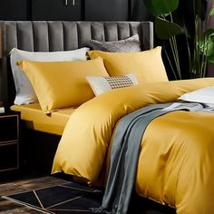 a bed with yellow sheets and pillows next to a potted green plant in the corner