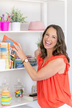 a woman in an orange top is smiling and looking at the books she's holding