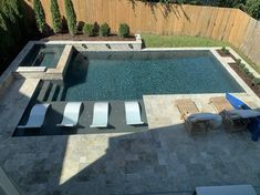 an aerial view of a pool and patio with lounge chairs in the foreground, next to a wooden fence