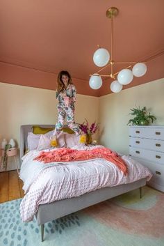 a woman standing on top of a bed in a room with pink walls and furniture