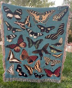 a blue blanket with many different butterflies on it in the grass next to a tree