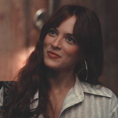 a woman with long brown hair and blue eyes is looking at the camera while wearing large hoop earrings