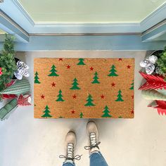 a person standing in front of a door mat with christmas trees on it