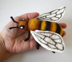 a hand holding a small felt bee on it's fingers, with its wings spread out