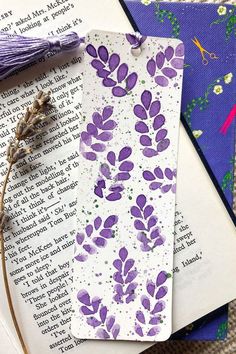 two bookmarks with purple flowers on them next to an open book and some scissors