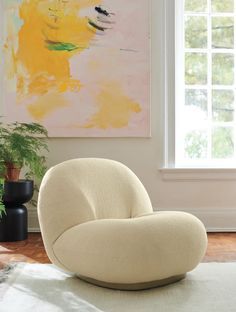 a white chair sitting on top of a rug in front of a window next to a potted plant