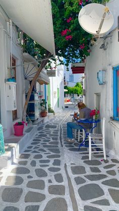 a person sitting on a chair in the middle of an alleyway with potted plants