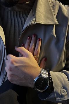 a woman with red nails is holding onto her watch while she's wearing a trench coat