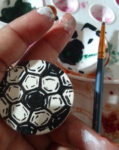 a hand holding a painted rock in front of some paintbrushes