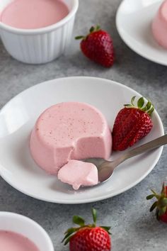 strawberry cheesecake on a white plate with strawberries around it and two cups of yogurt in the background