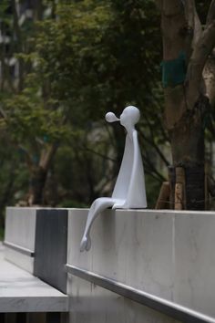 a white sculpture sitting on top of a cement wall next to a tree and sidewalk