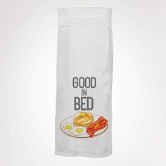 a dish towel that says good in bed with bacon and eggs on the plate next to it