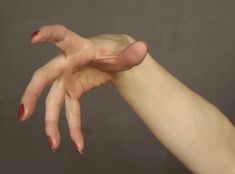 a woman's hand with red nail polish holding onto her left arm, against a gray background