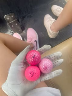 three pink golf balls are in the palm of a person's hand, with white gloves on