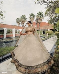 a woman in a white and gold bridal gown standing on a walkway with palm trees behind her