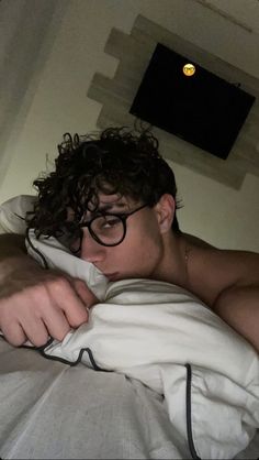 a man with glasses laying in bed under a blanket