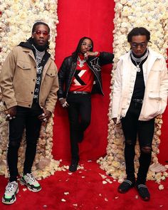 two men standing next to each other in front of a red wall with flowers on it