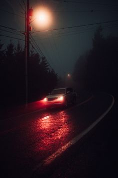 a car driving down the road at night with its headlights on and fog in the air