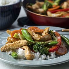 chicken, broccoli, peppers and rice on a plate with a bowl of rice in the background