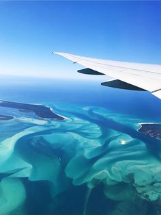 an airplane wing is flying over the ocean and landforms that are blue in color