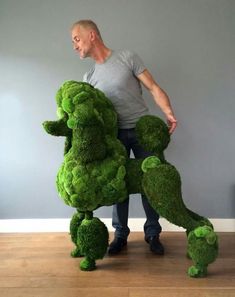 a man standing next to a giant green dog made out of fake flowers and grass