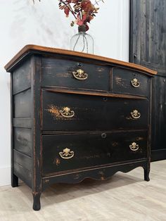 an old black dresser with gold handles and knobs on the drawers is next to a vase with flowers in it