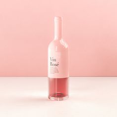 a bottle of pink wine sitting on top of a white table next to a pink wall