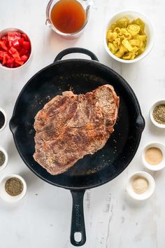 steak in a skillet with spices and seasonings around it on a white table