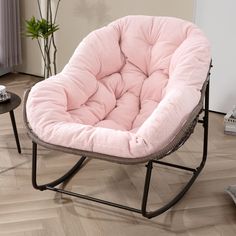 a pink chair sitting on top of a hard wood floor next to a table with a potted plant