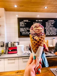 a person holding up an ice cream cone in front of a counter with menus on it