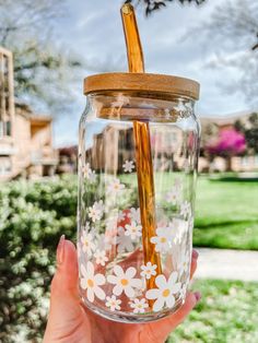 a hand holding a glass jar with flowers painted on it and a straw sticking out of the top