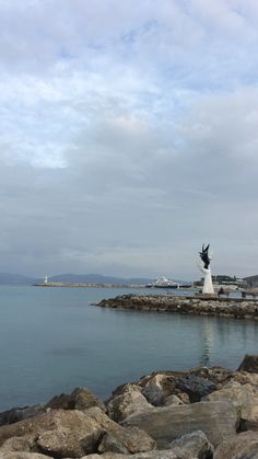 there is a statue in the middle of some rocks by the water and buildings on the other side