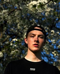 a young man standing in front of a tree with white flowers