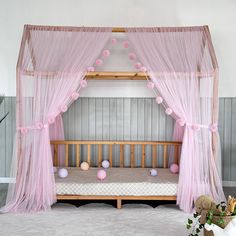 a pink canopy bed with sheer curtains and balls on the floor in front of it