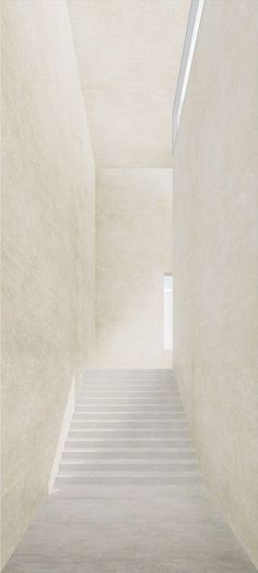 an empty staircase leading up to the skylight in a white room with concrete walls