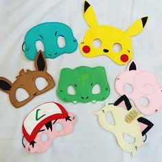 five masks with different designs on them sitting on a white cloth covered surface, one has a pikachu mask and the other has a pokemon mask