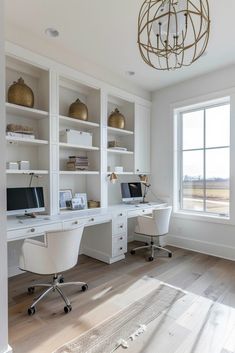 a home office with built in desks and white bookcases, along with a chandelier