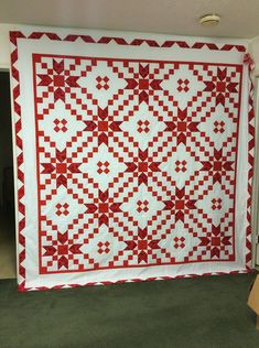 a large red and white quilt hanging from the ceiling in a room with green carpeting