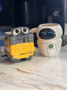 two toy cars sitting on top of a counter next to a coffee cup with eyes