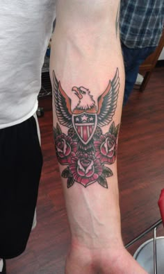 a person with a tattoo on their arm that has an eagle and roses around it