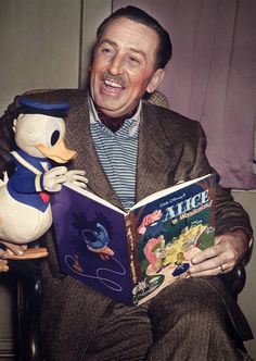 a man sitting in a chair reading a book with a ducky stuffed animal next to him