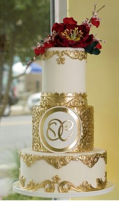 a three tiered white and gold wedding cake with red flowers on the top layer