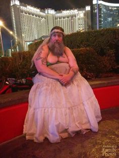 a man in a wedding dress sitting on a red bench with his arms folded out