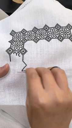 someone is stitching on a piece of white fabric with blackwork in the shape of an ornament