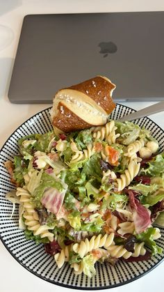 a plate with some pasta salad and a sandwich on it next to an apple laptop