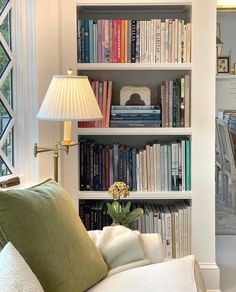 a living room filled with lots of books on top of a white book shelf next to a window