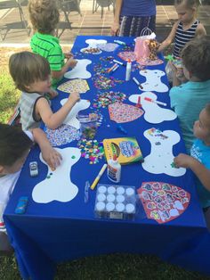 a group of children sitting at a table with paper plates and paintbrushes on it