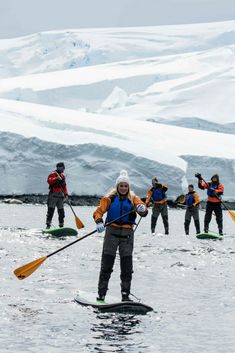 a group of people paddling on surfboards in the water with snow covered mountains behind them