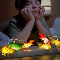 a young boy sitting at a table with some toy dinosaurs on top of it and lights in the background