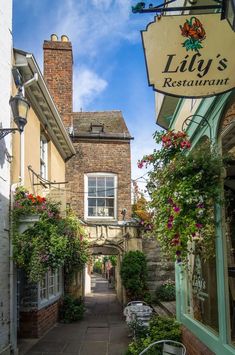 an alley way with flowers growing on the side of it and a sign that says lily's restaurant